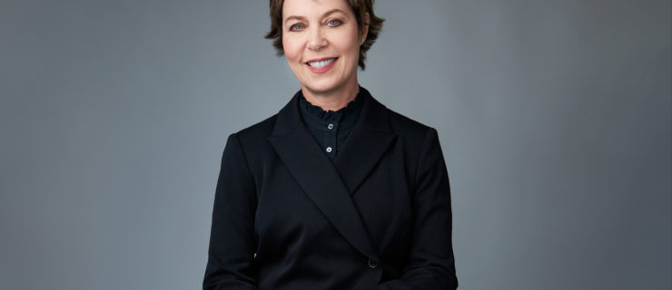 Susan Jaffe is a fair-skinned white woman with short dark hair. She wears a dark suit and seated, facing the camera and smiling.