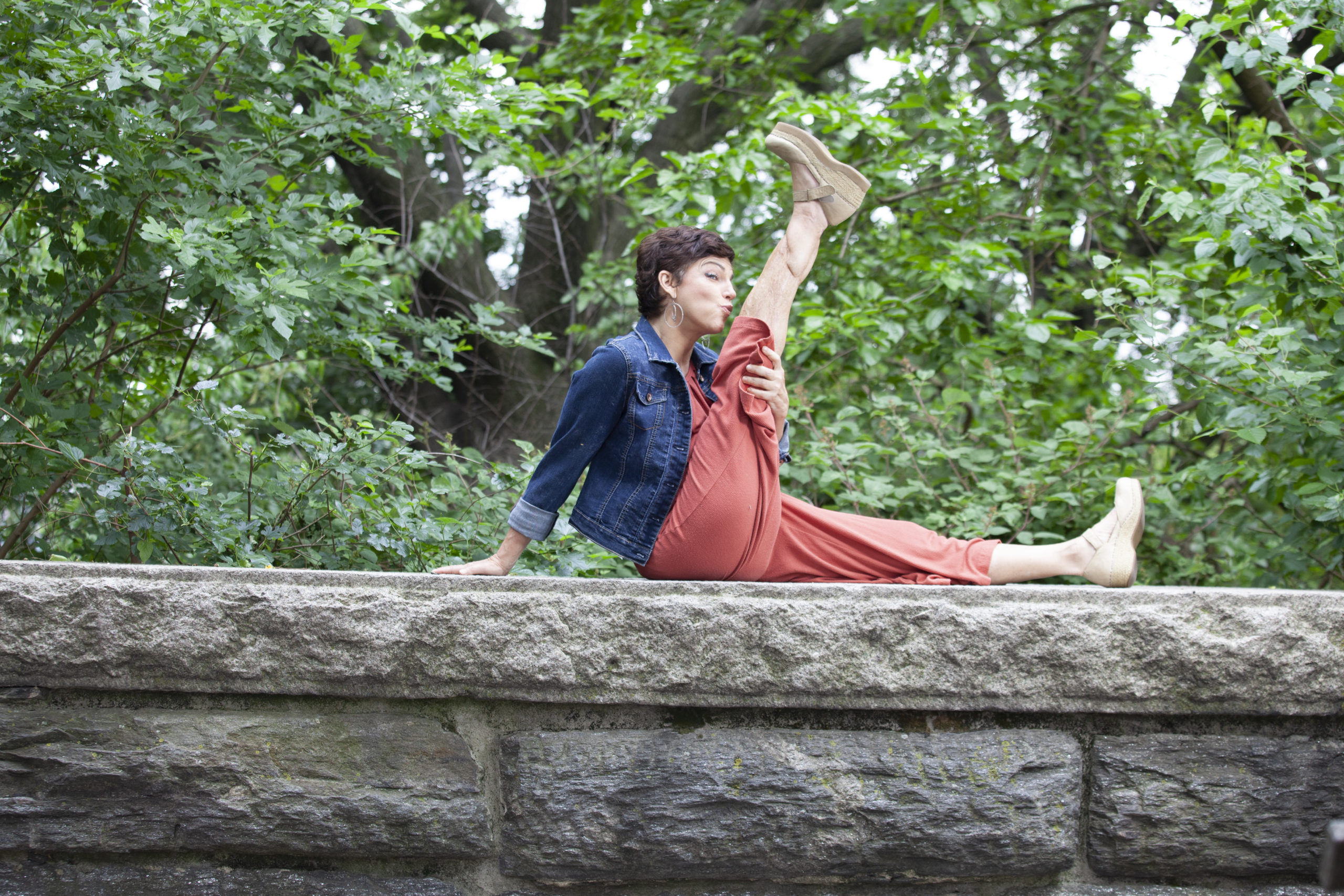 Amy Jordan sits atop a stone wall, her right leg extended upwards as she leans in to kiss her knee.