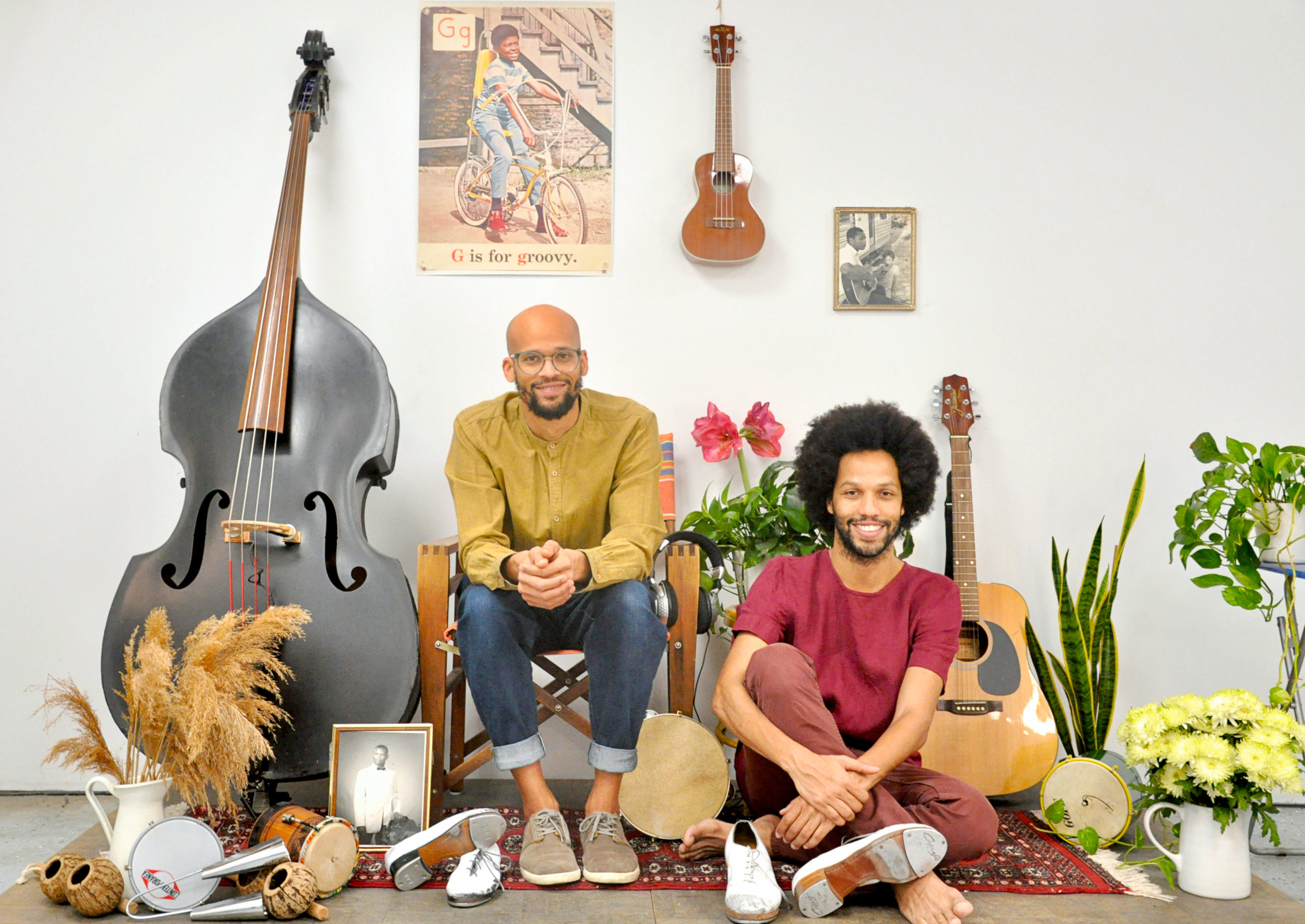 Gregory Richardson is a light-skinned Black man who is bald and has a beard and glasses. Leonardo Sandoval is a man with a medium complexion, curly hair and a beard. They sit on a carpet surround by musical instruments.