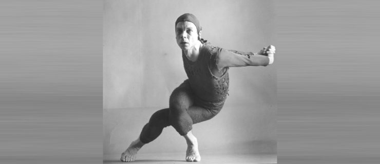 In a black and white archival image, Merce Cunningham poses in a textured unitard and stocking cap. His arms are extended behind him, hands clasped. His legs are twisted and crossed as though sitting in a chair, but he balances on the balls of his feet, knees deeply bent, upper body curved but elongated.