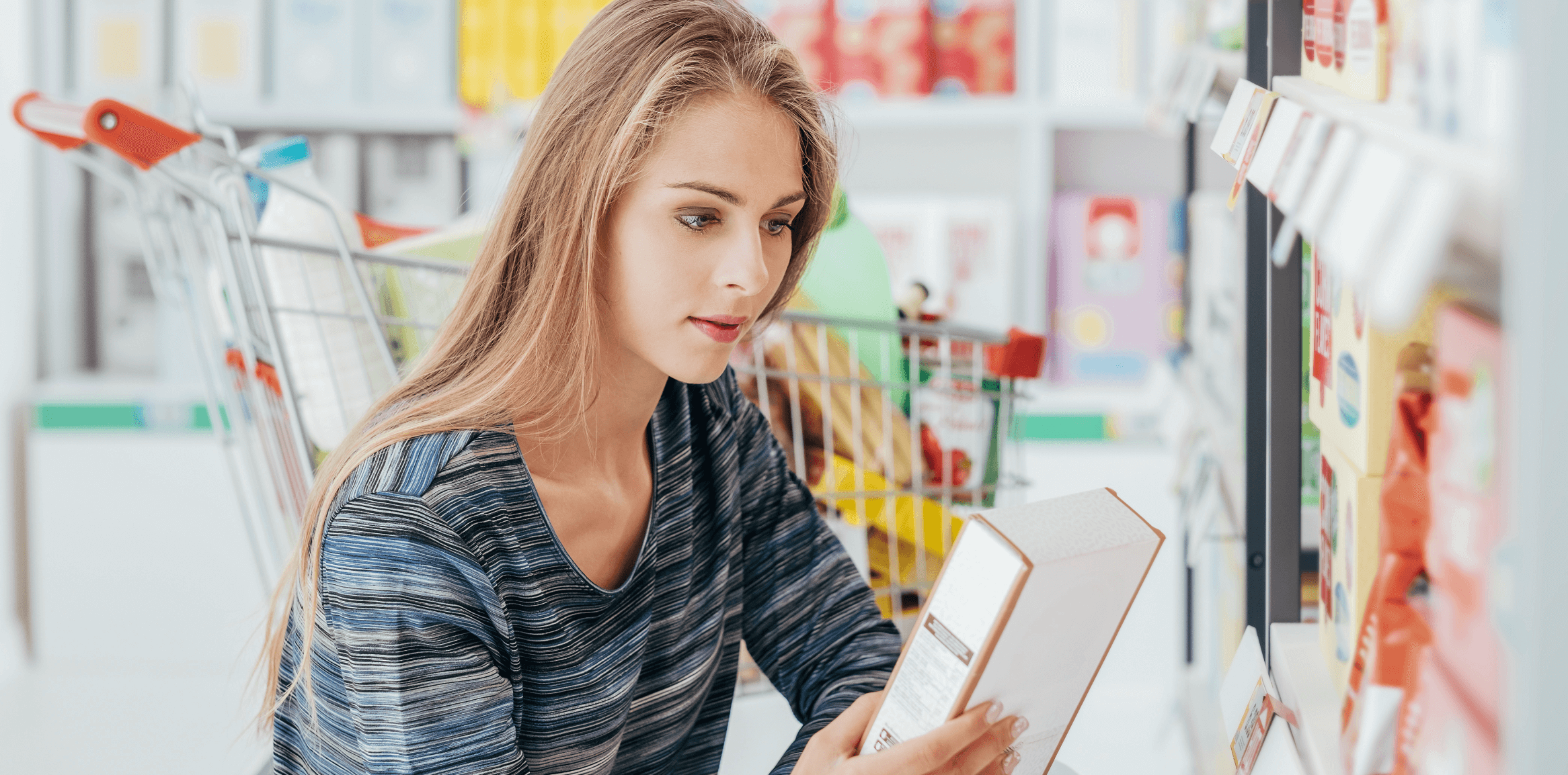 A blonde, fare-skinned woman in a grocery store looks closely at a cereal box.