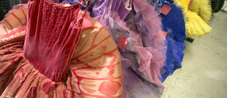 Ballet tutus in rainbow colors hang on a garment rack.