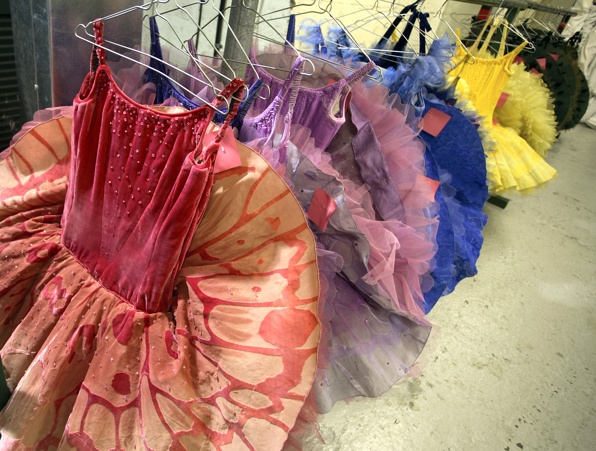 Ballet tutus in rainbow colors hang on a garment rack.