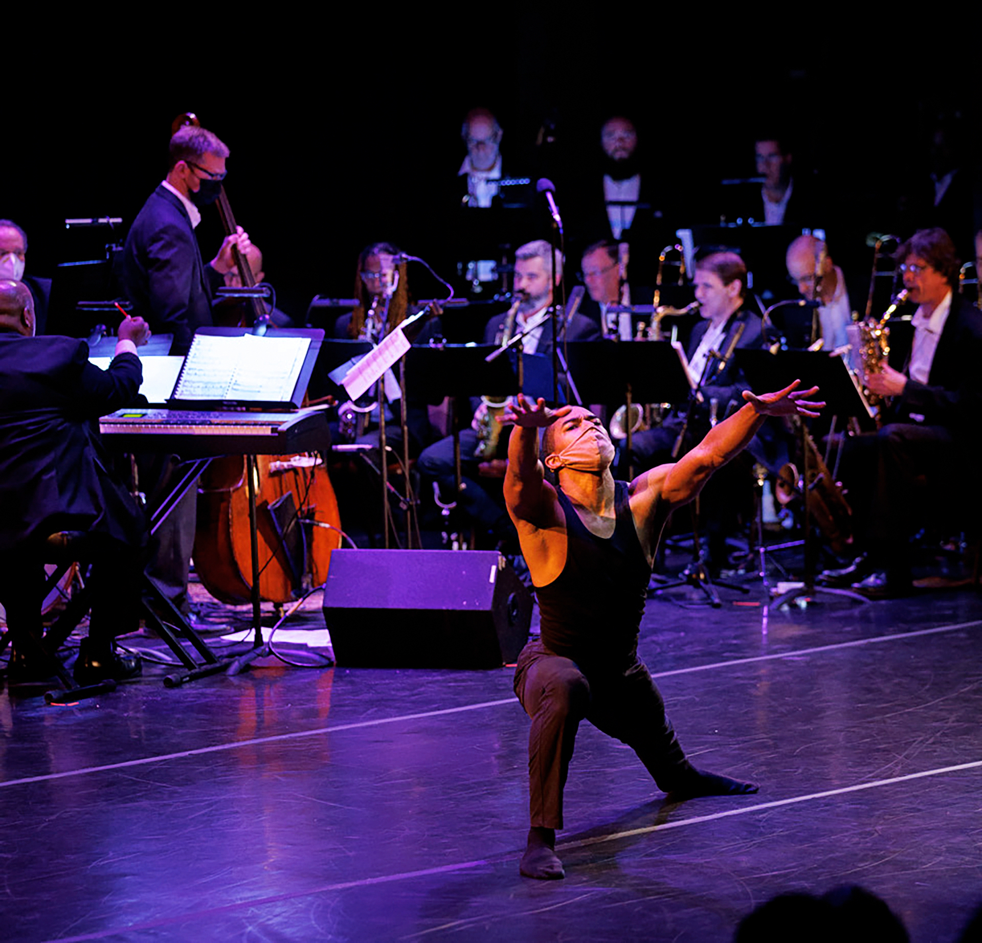 dancer lunging and reaching forward, orchestra playing behind him