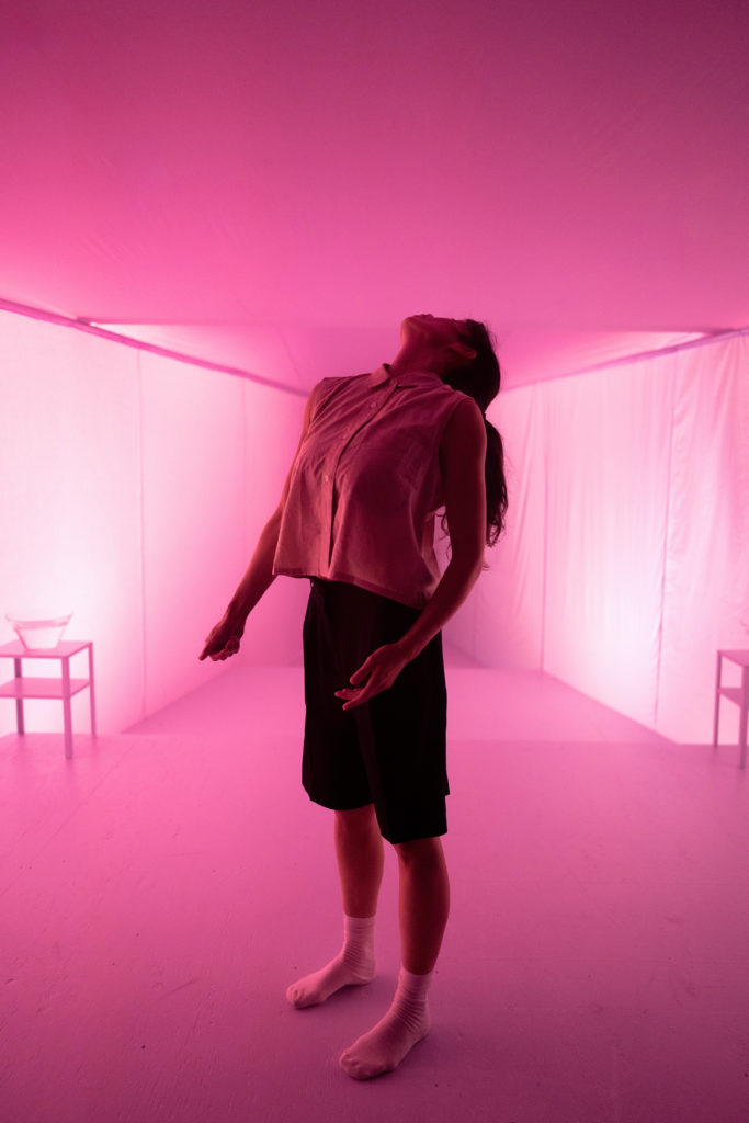 female dancer looking up in a pink lit room 