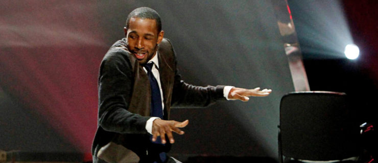Stephen "tWitch" Boss glances over his shoulder toward Hayley Erbert as they perform onstage. He shoulders are raised, elbows bent and palms down as though they are raising his left knee, puppet-like.