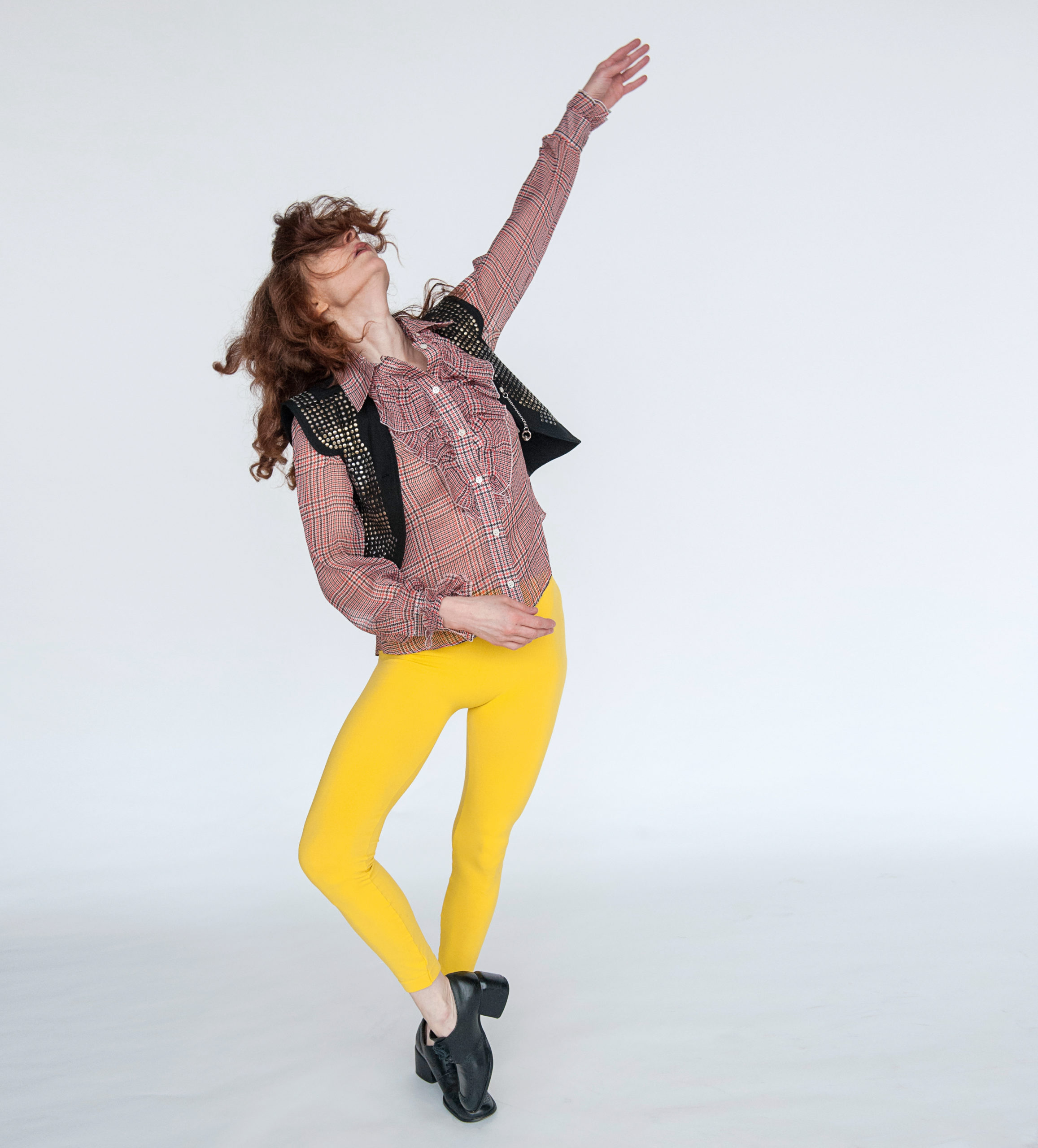 woman in yellow pants and plaid shirt, one arm up one foot in coupe