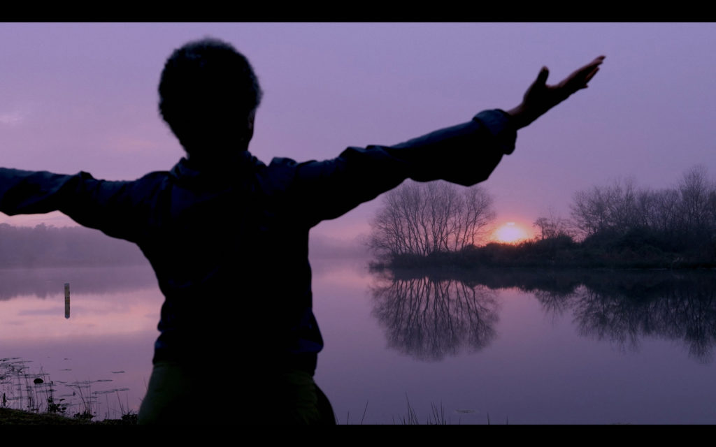 dancer with arms spread wide overlooking lake at dusk