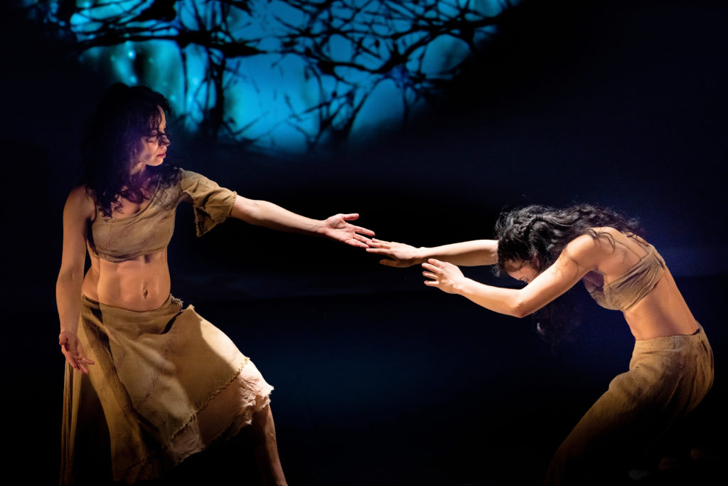 two female dancers reaching for each other, only finger tips touching 