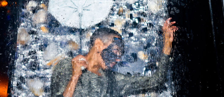 dancer under waterfall wearing grey shirt and mask, holding an umbrella