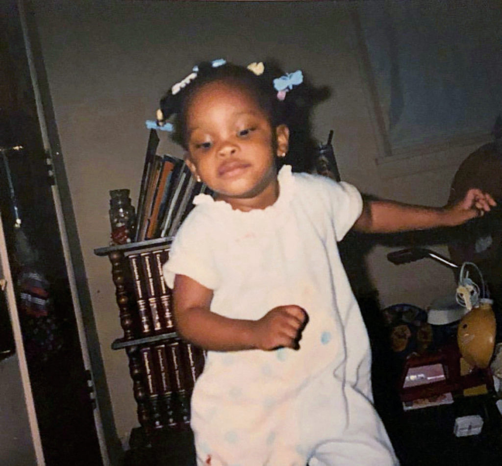 Charm La'Donna as a toddler. Her expression is serious as she dances by herself at home.