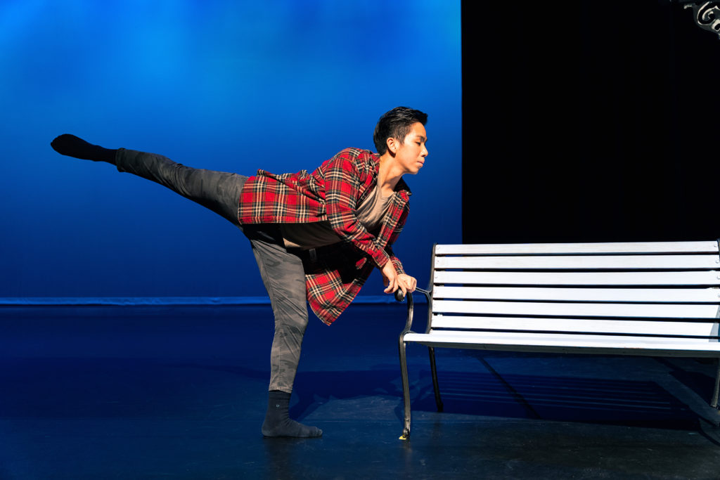 male dancer leaning on bench performing arabesque 