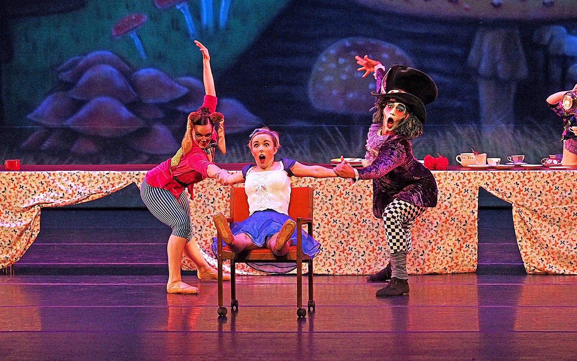 female looking surprised sitting a chair holding hands with two other dancers 