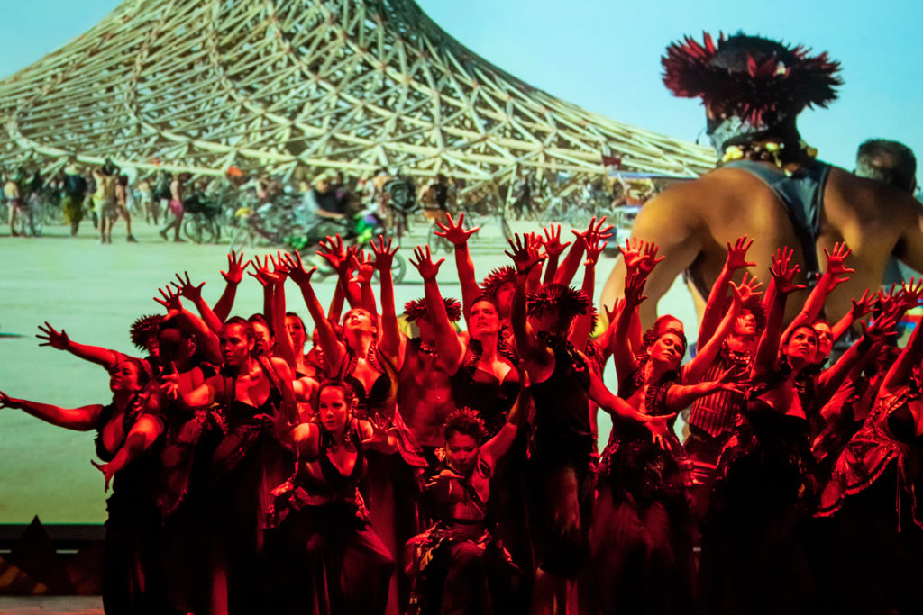 large group of dancers performing in front of large screen 