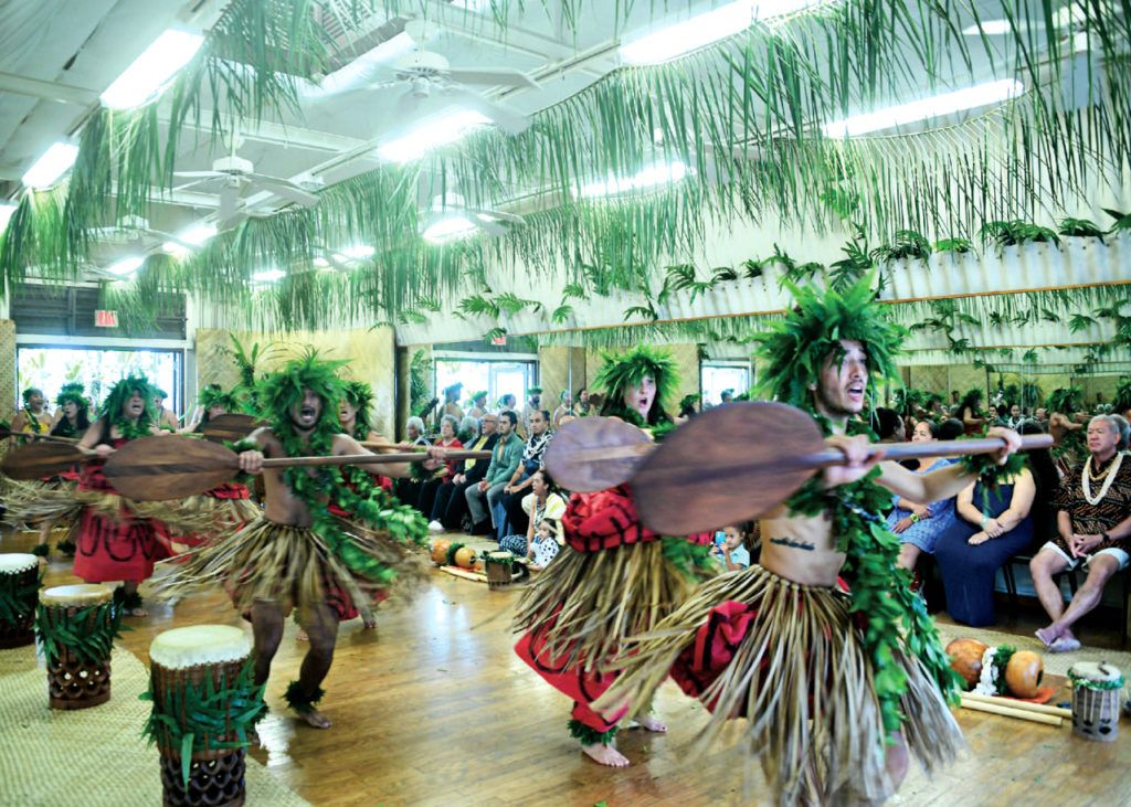 dancers performing in a studio wearing traditional costumes holding paddles