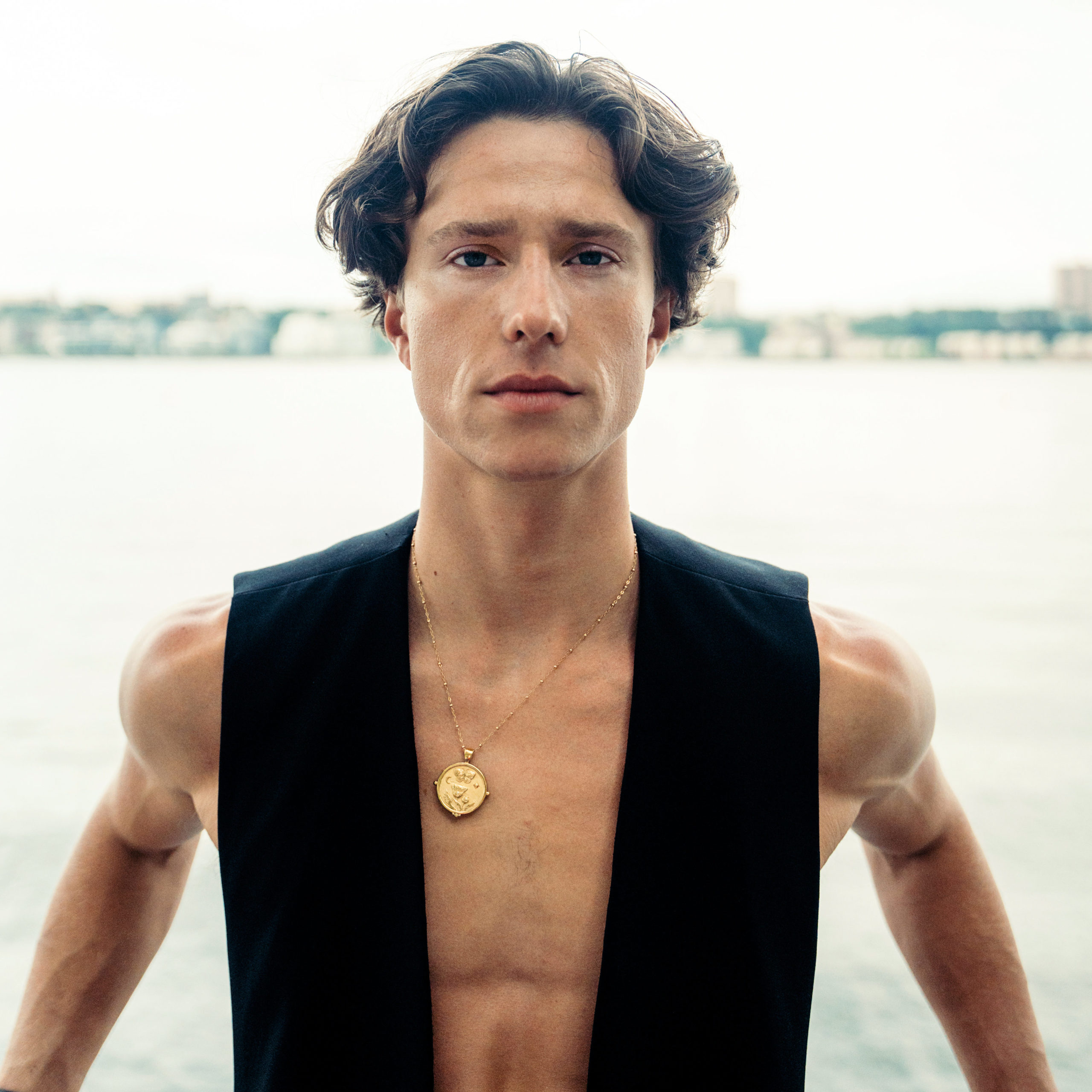 male dancer wearing black vest and gold necklace staring at camera