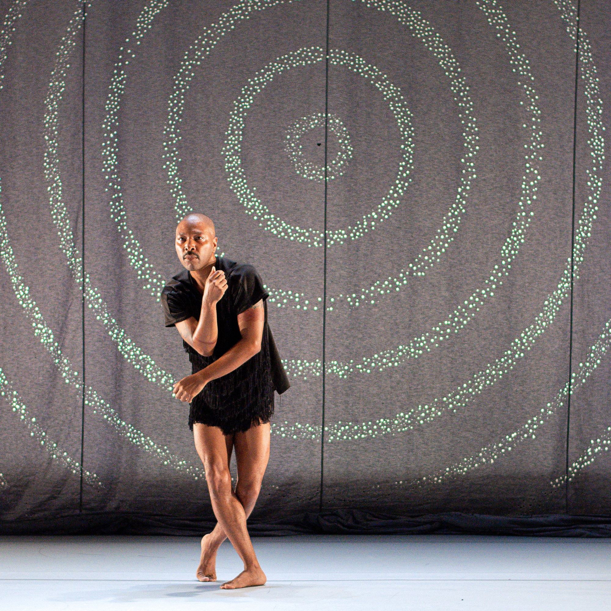 male dancer wearing black t shirt dancing in front of a spiral backdrop 