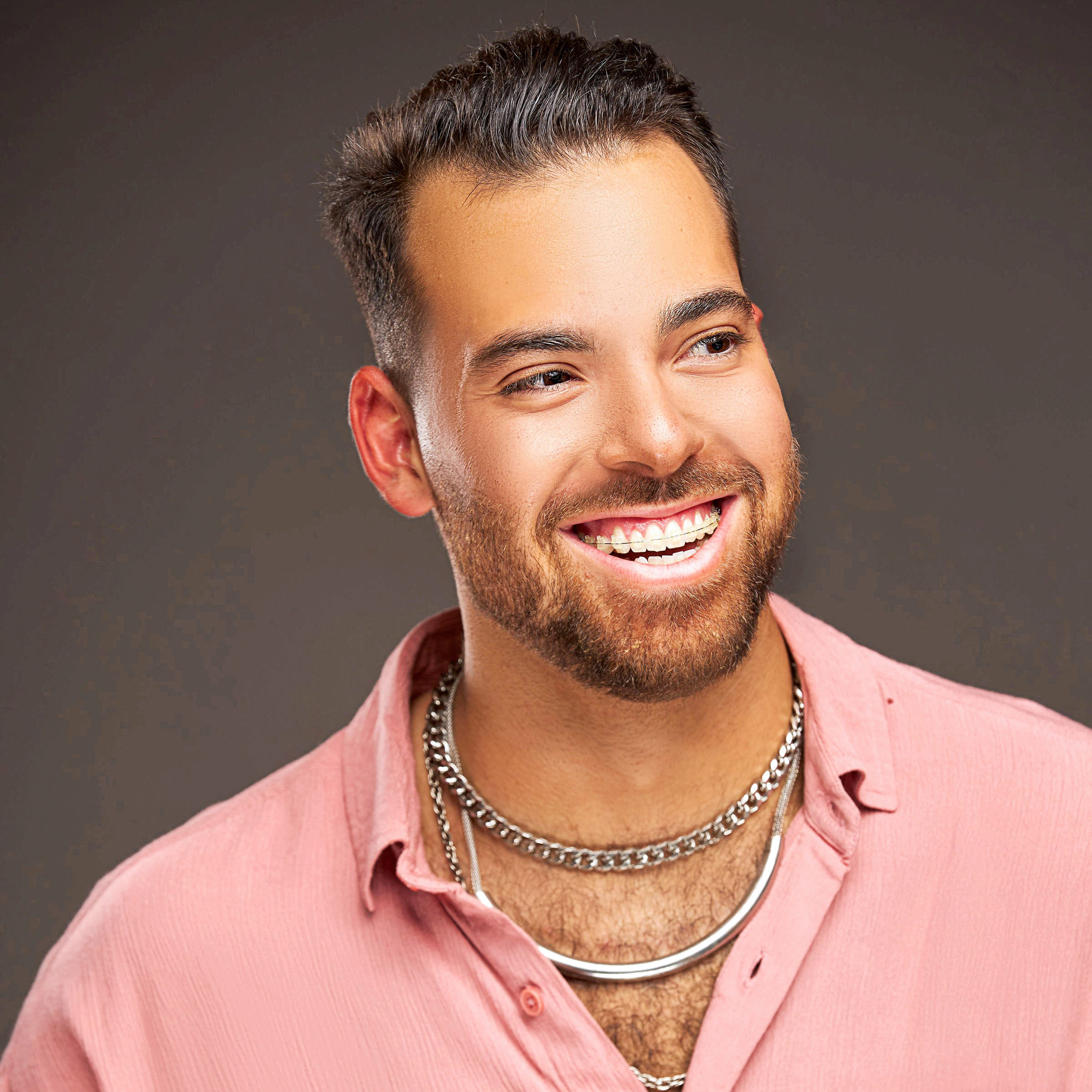 male wearing silver necklaces and pink collared shirt 