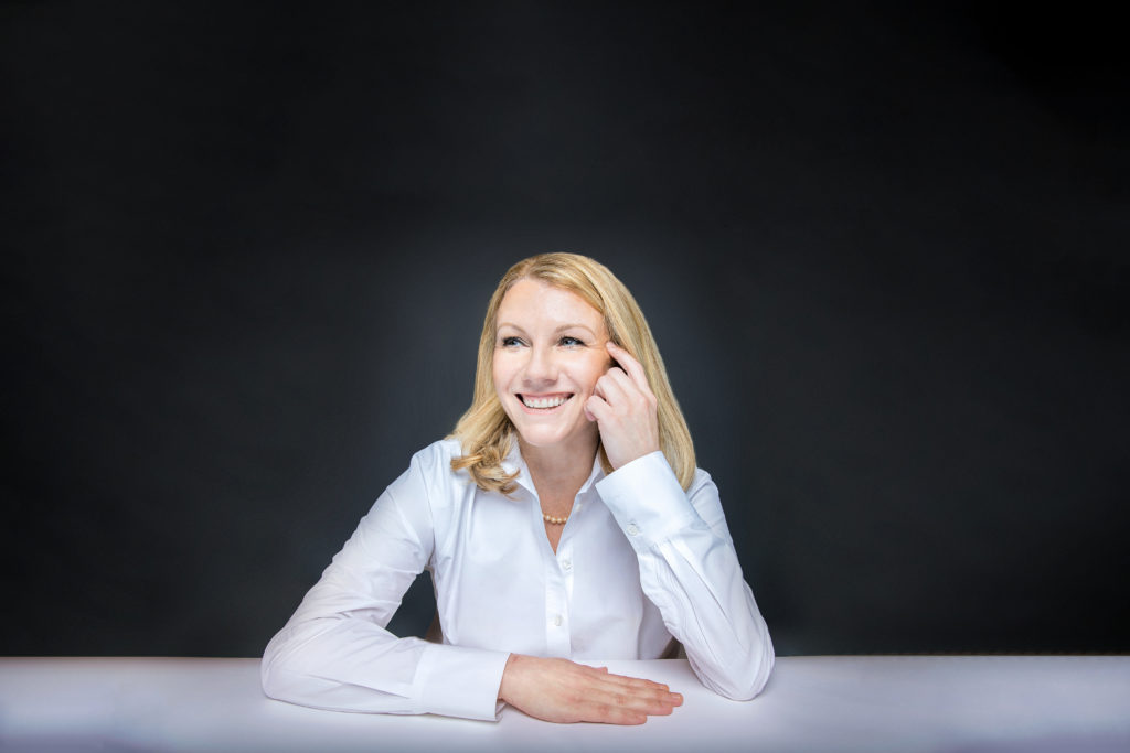 blonde female sitting at a table wearing a white button down shirt