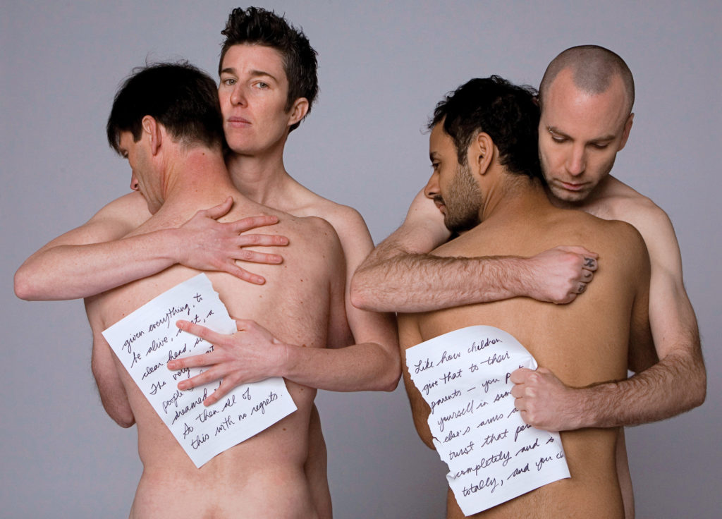 4 males hugging and holding paper with writing 