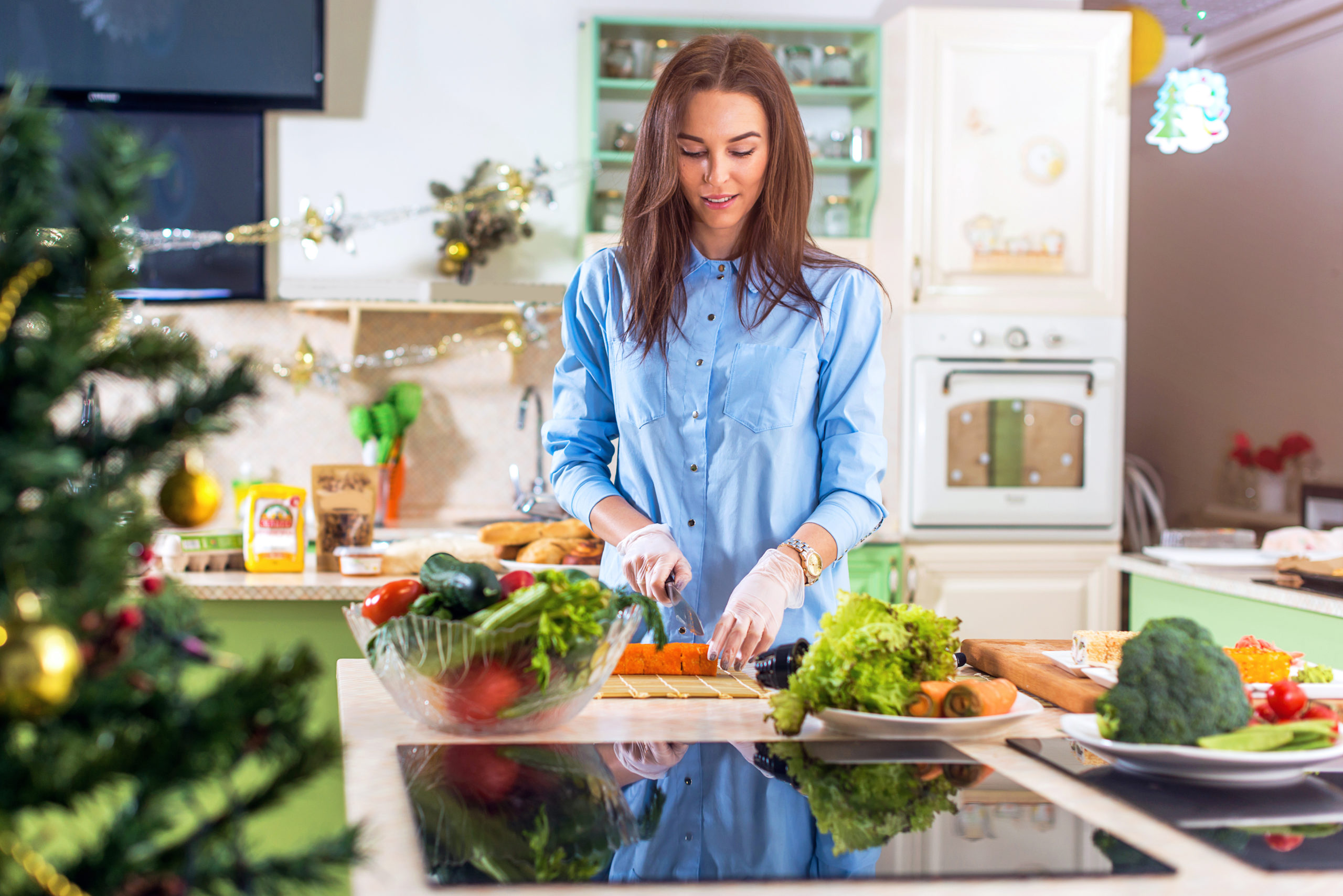 Female wearing blue button down chopping vegetables in the kitchen