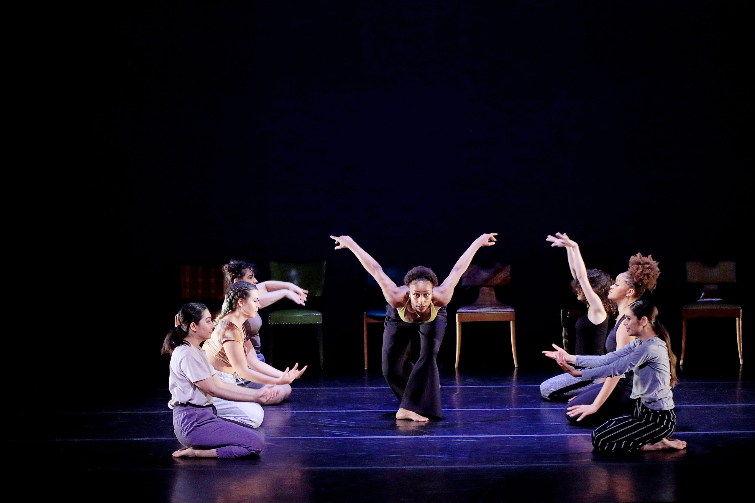female dancer bowing forward in center with other dancers kneeling on either side of her
