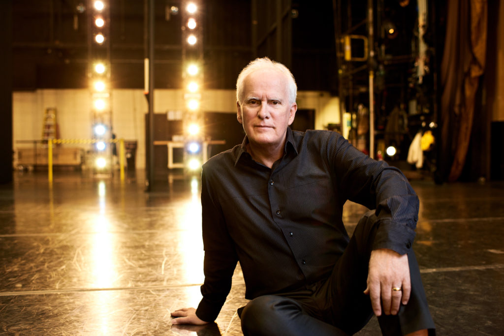 male sitting on the floor of a stage wearing all black 