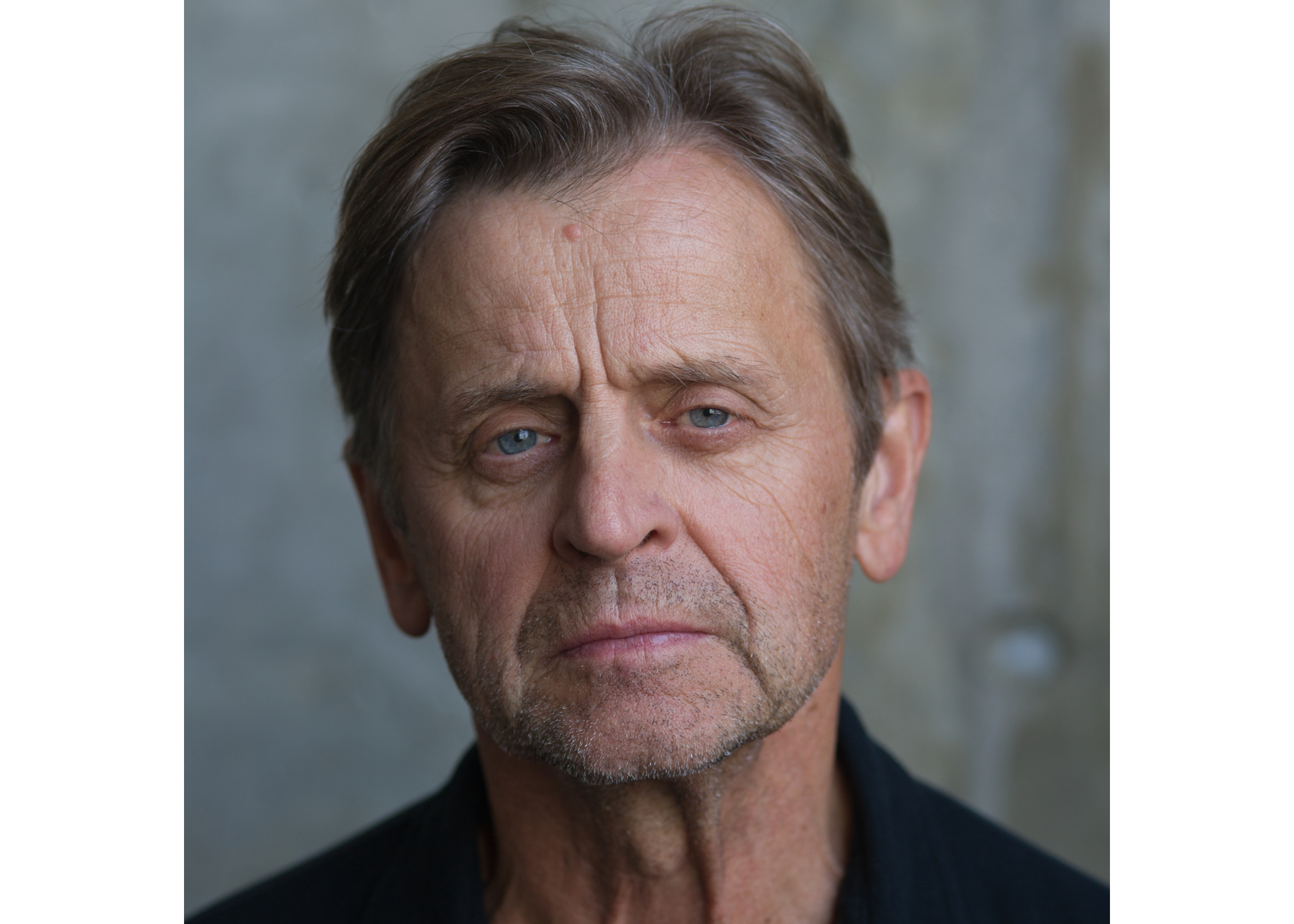 Mikhail Baryshnikov's head and shoulders in a blue shirt on a grey background.