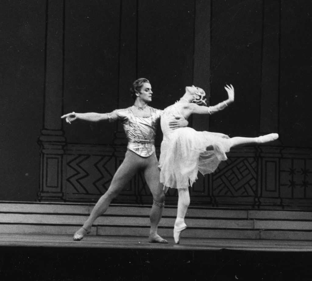 In this black and white photo, Mikhail Baryshnikov holds Leslie Collier by the waist as she leans back in an arabesque onstage."