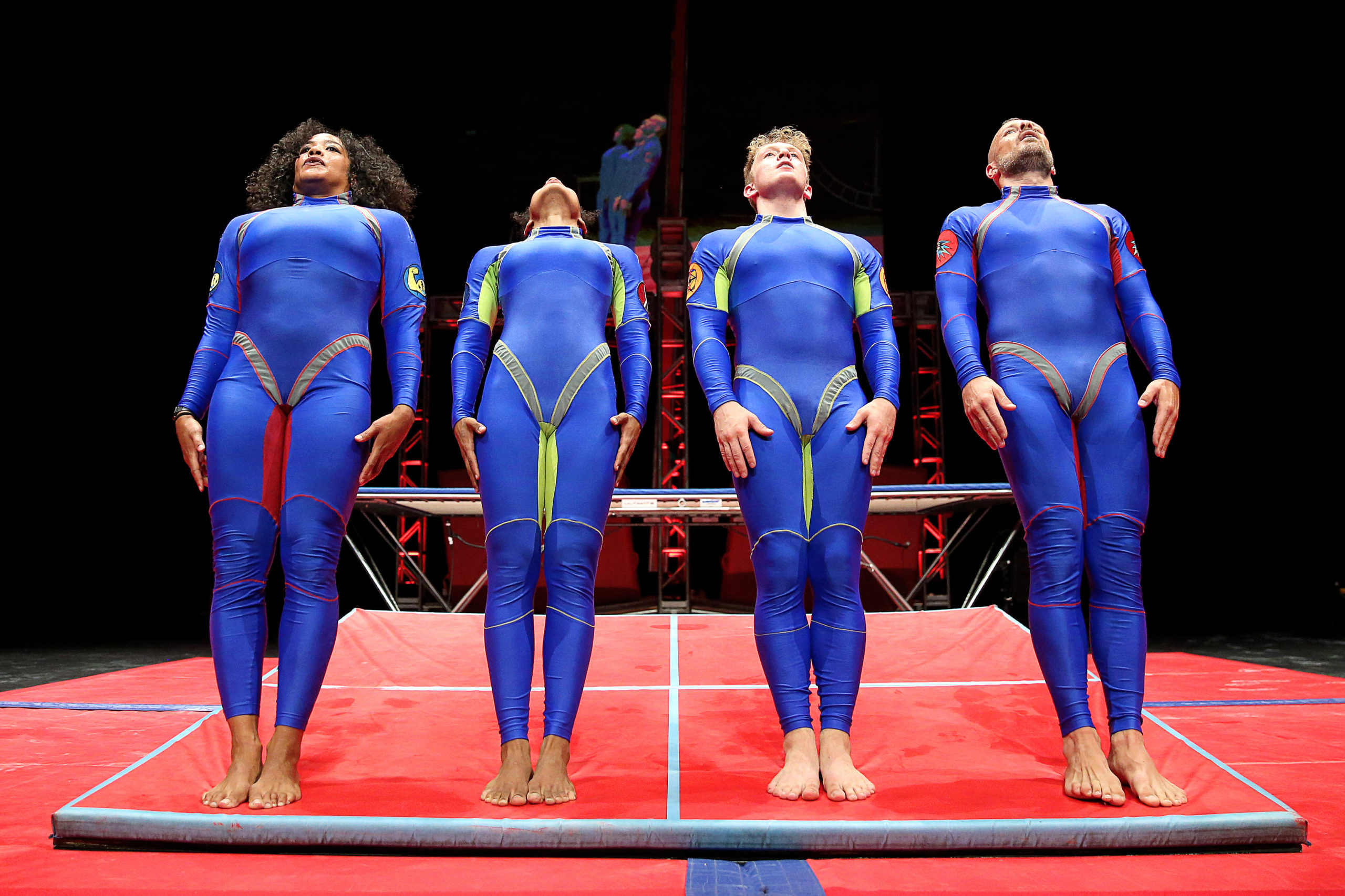 4 dancers wearing blue body suits leaning backwards