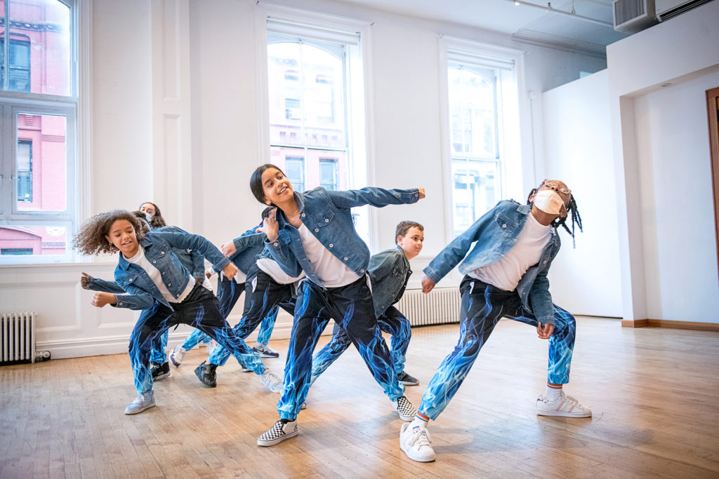 a group of kids wearing jean jackets and blue pants dancing in a studio