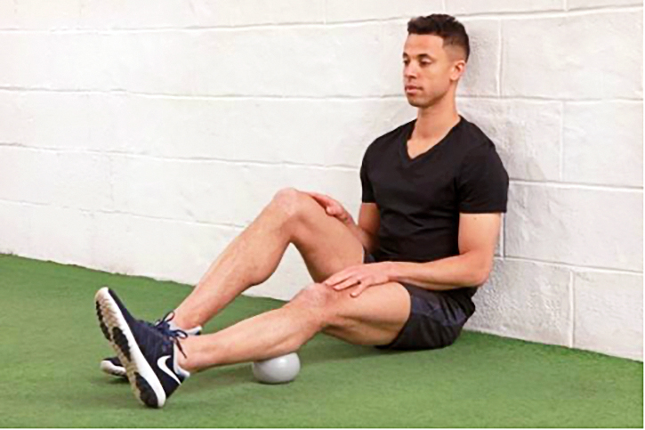 male sitting on floor massaging calf with ball