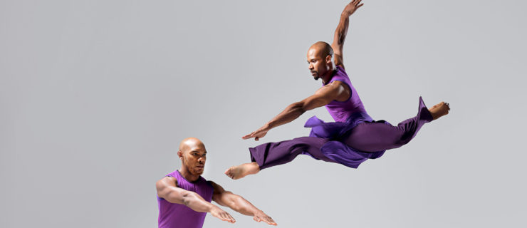 two male dancers wearing purple, one jumping the other lunging