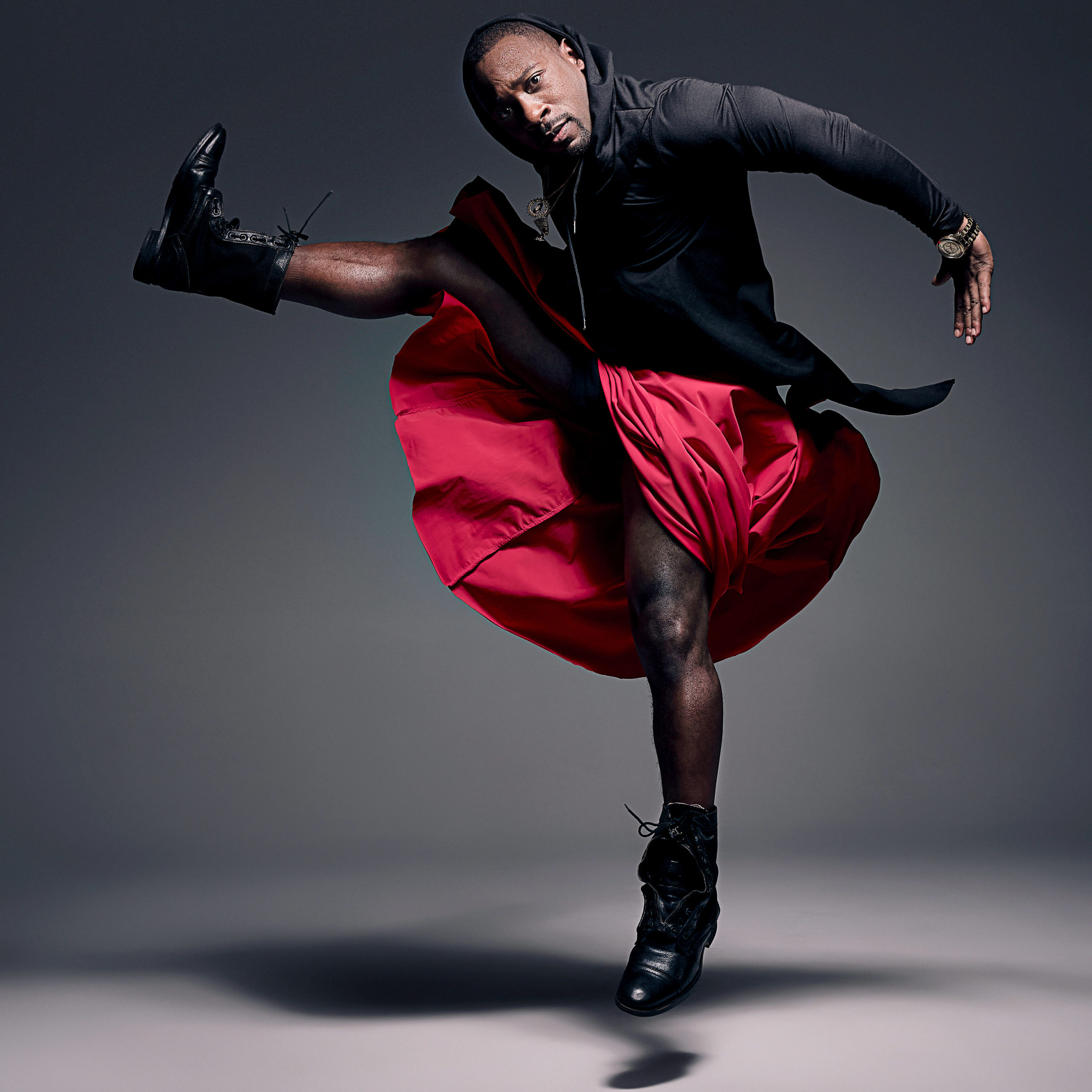 male dancer wearing black zip up and red skirt jumping