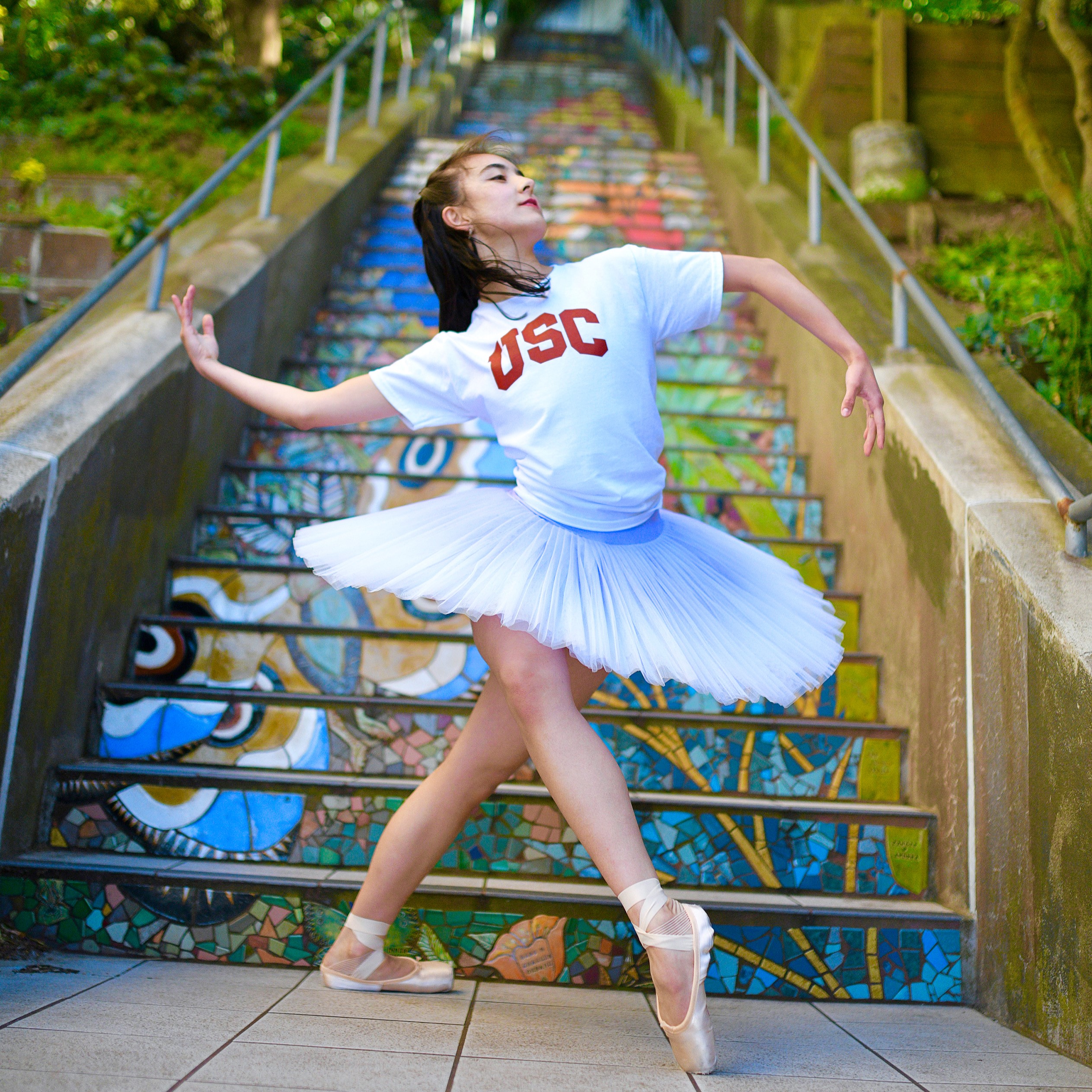 female dancer wearing a tutu and USC shirt dancing in front of mosaic stairs
