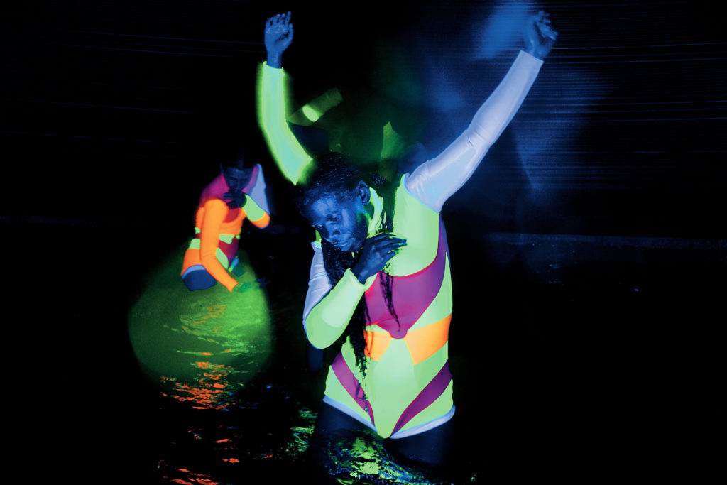 male dancer wearing neo glowing bodysuit performing in water