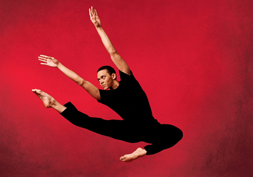 male dancer jumping in front of red background 