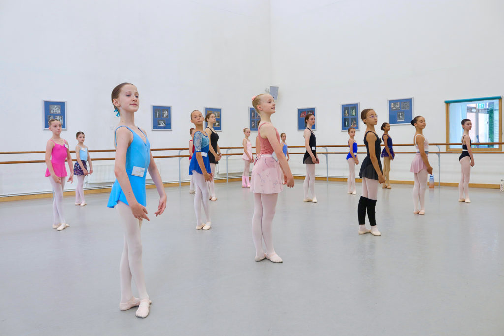 a large group of female dancers in a studio standing in 5th position 