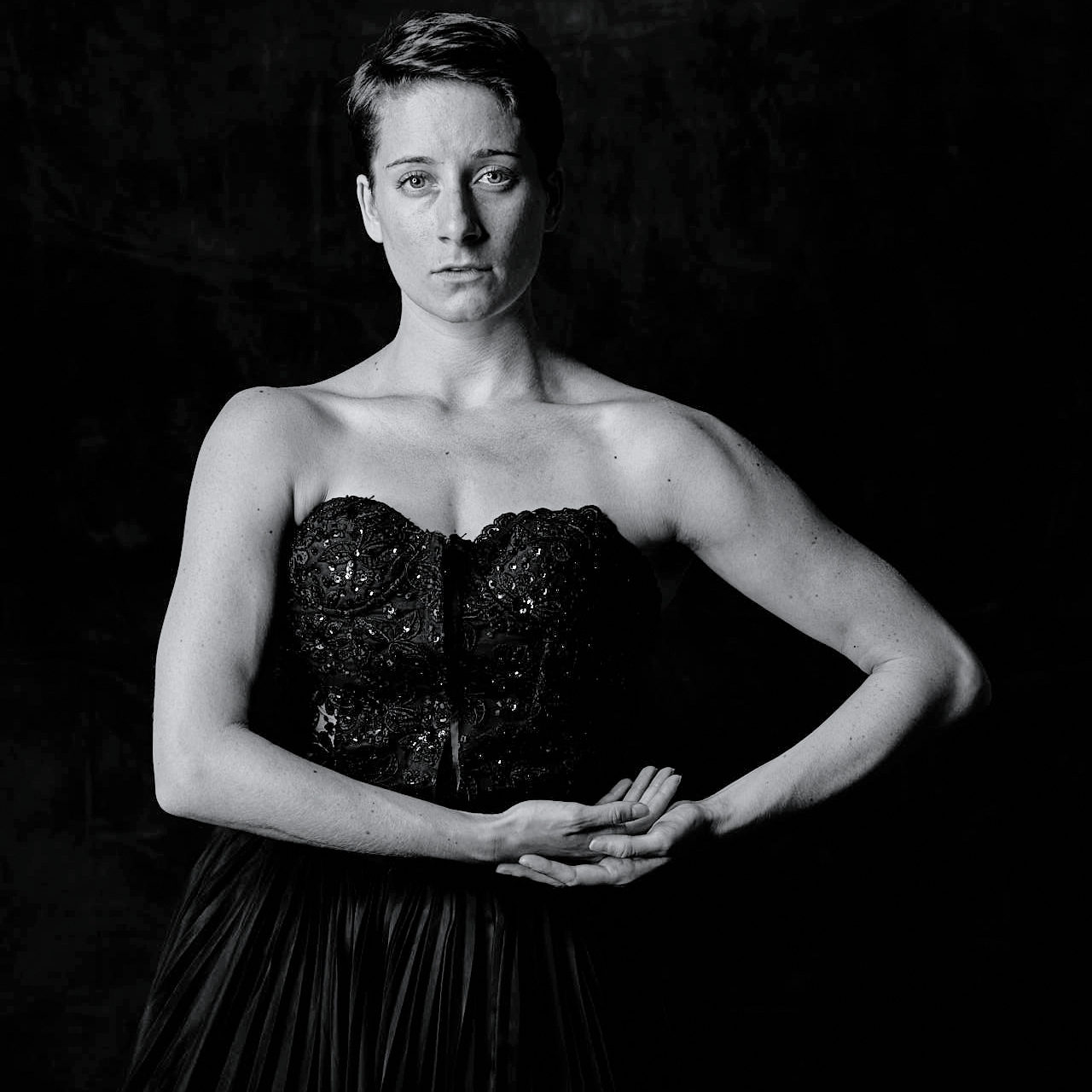 a female dancer wearing a strapless black dress looks at the camera