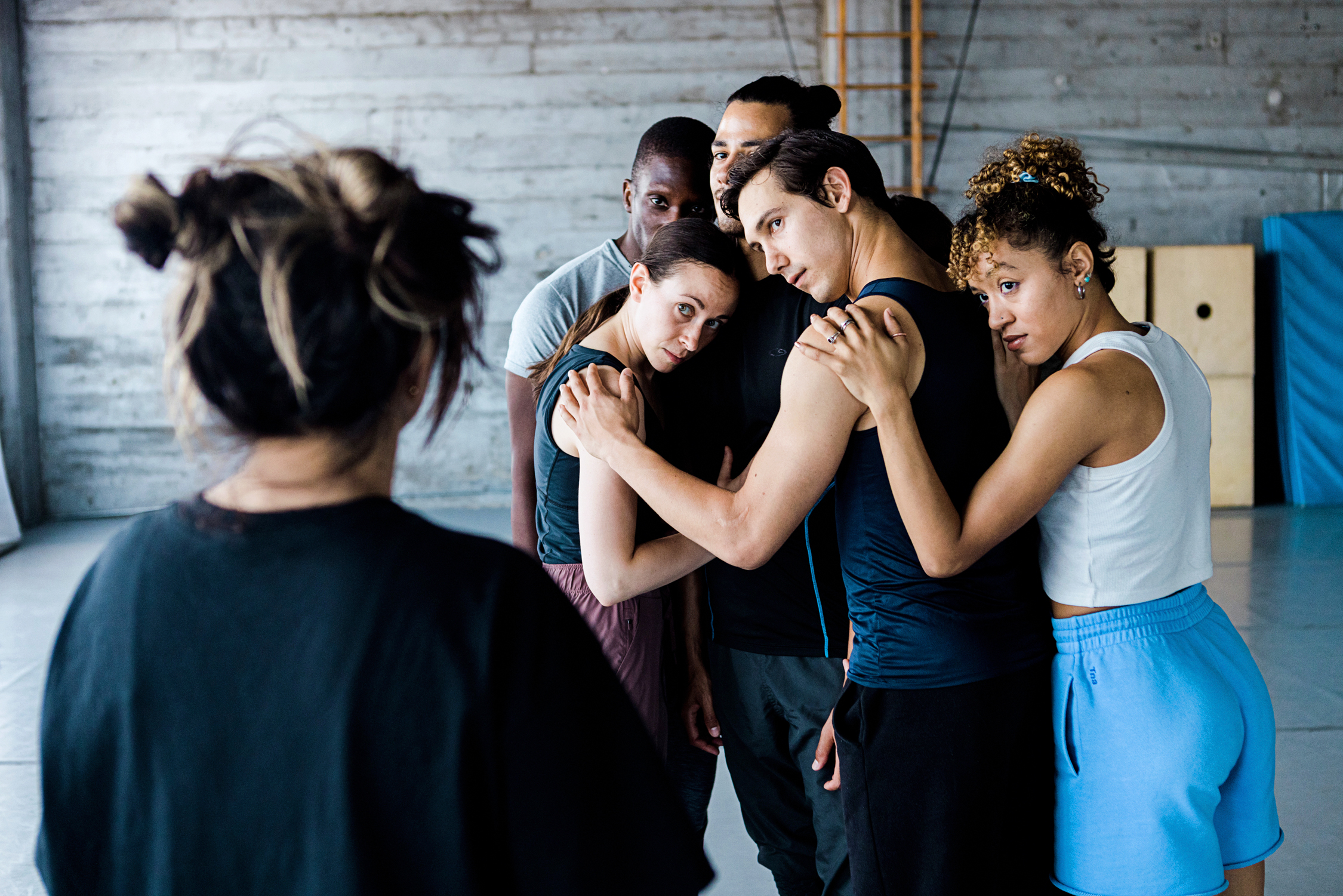five dancers hugging each other looking at a woman in the front of the room