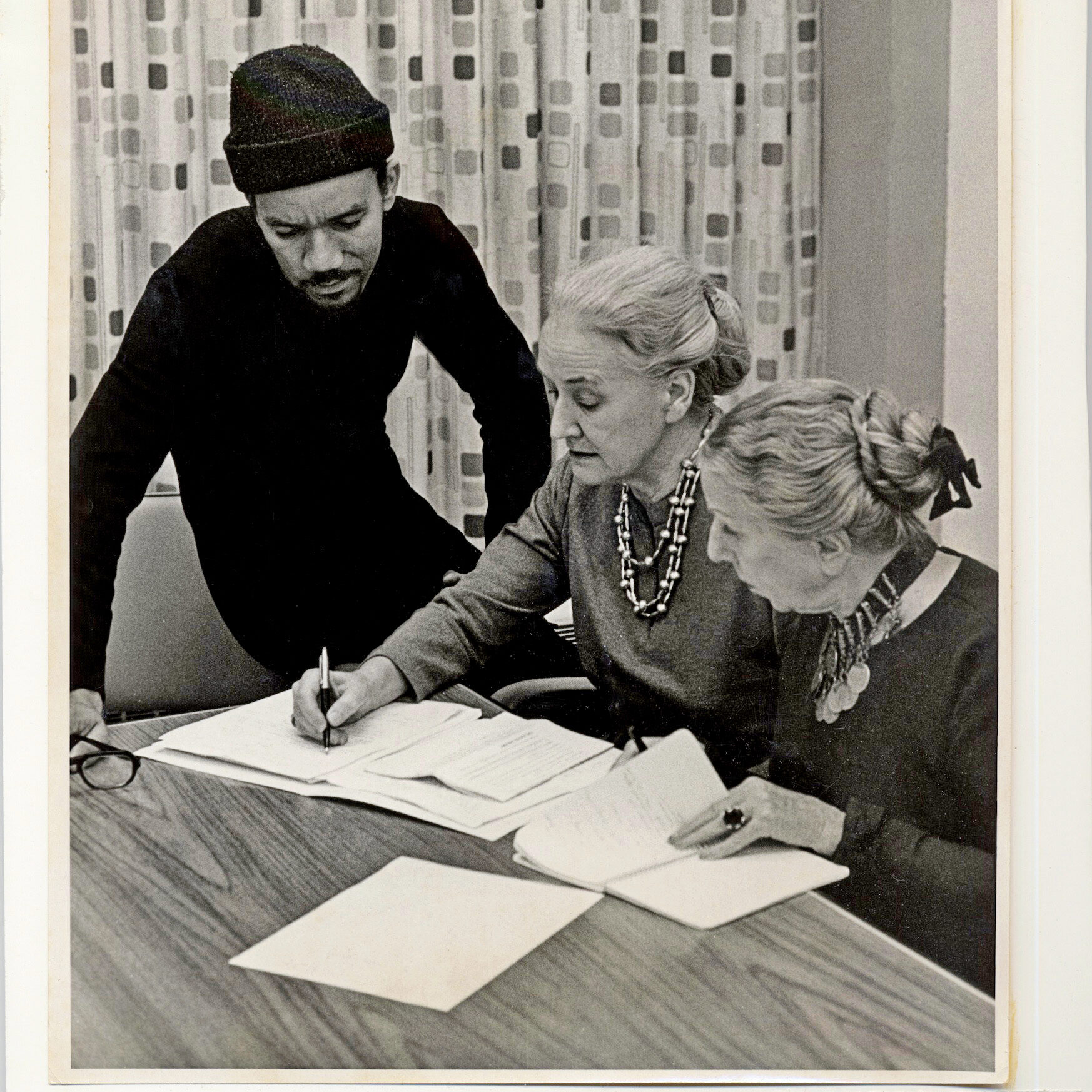 one man and two women at a table looking at a notebook