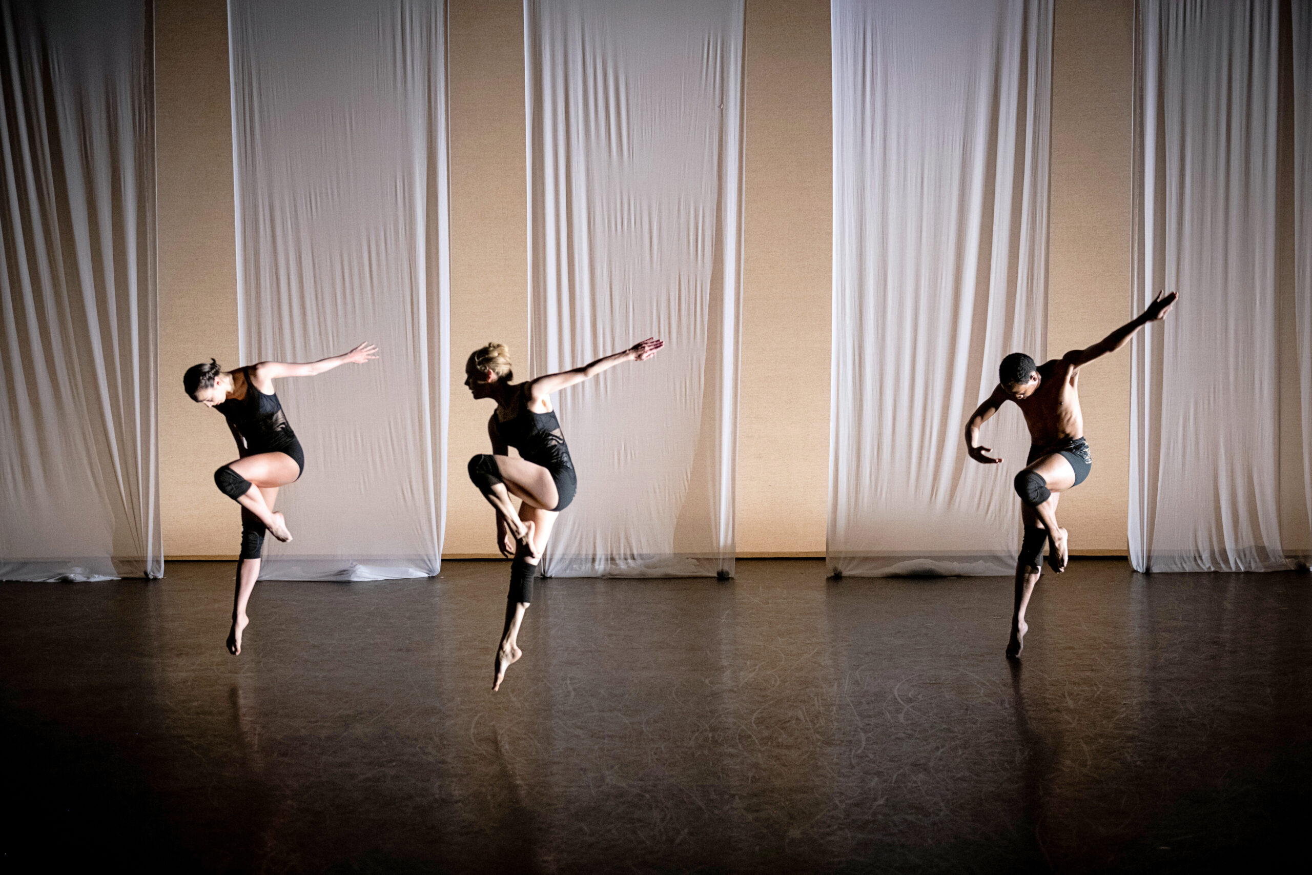 three dancer jumping in parallel passe with one arms swinging back
