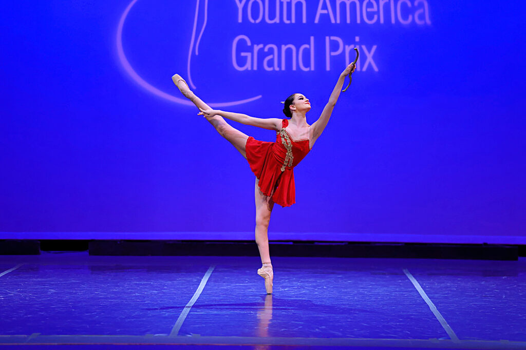 female dancer in red dress performing an arabesque on stage