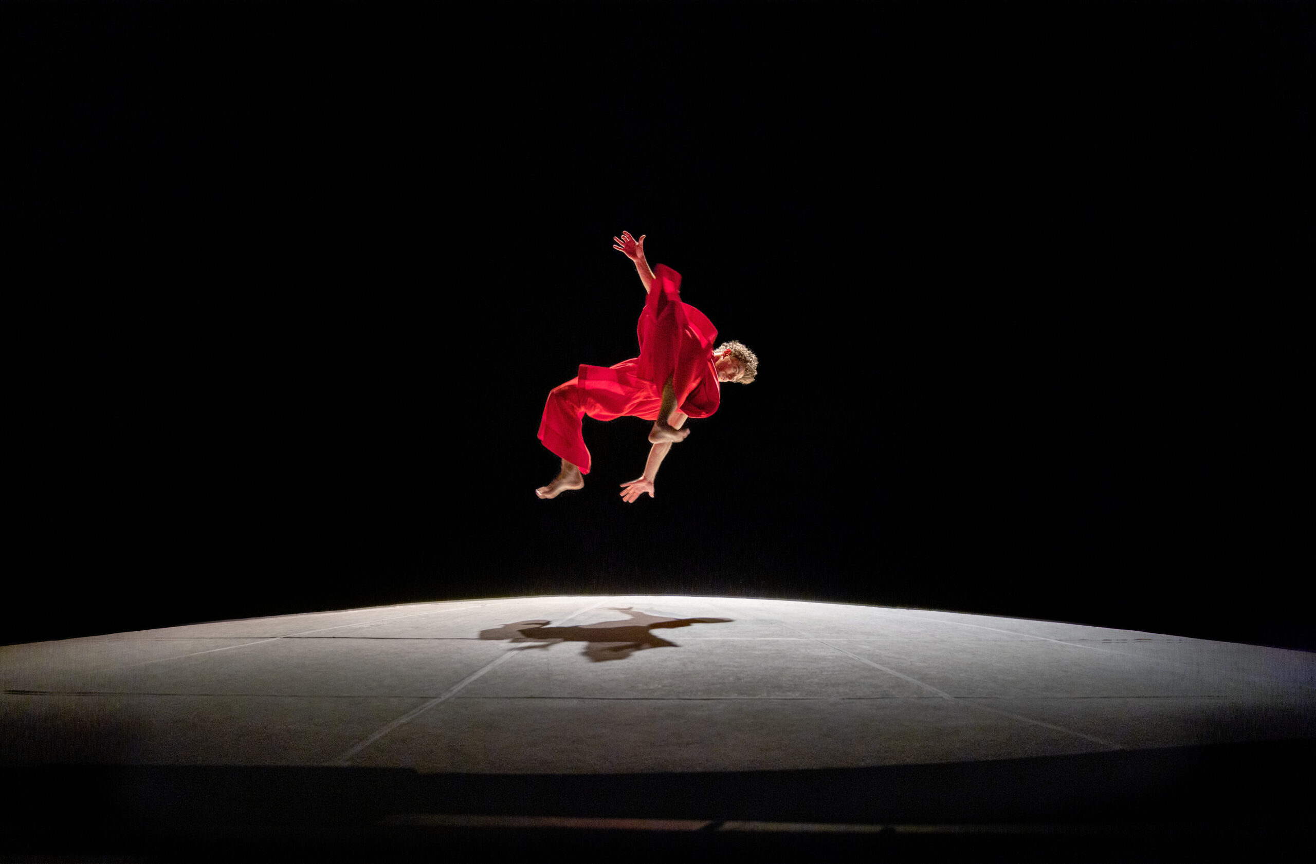 male dancer wearing red flowy costume flying through the air