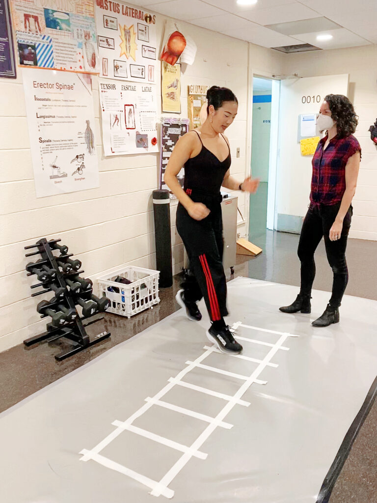 female trainer coaching dancer through footwork exercise using layout of floor