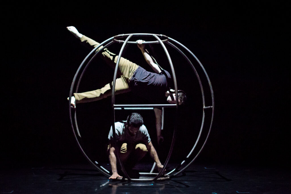 two dancers inside a large metal circular sculpture