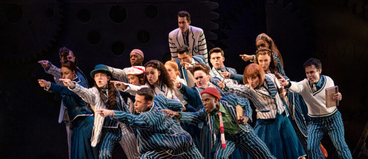 a large group of performers wearing striped suits pointing towards the corner of the stage