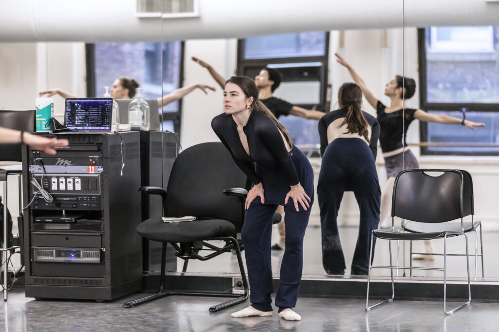 female choreographer wearing all black watching three dancers in a studio
