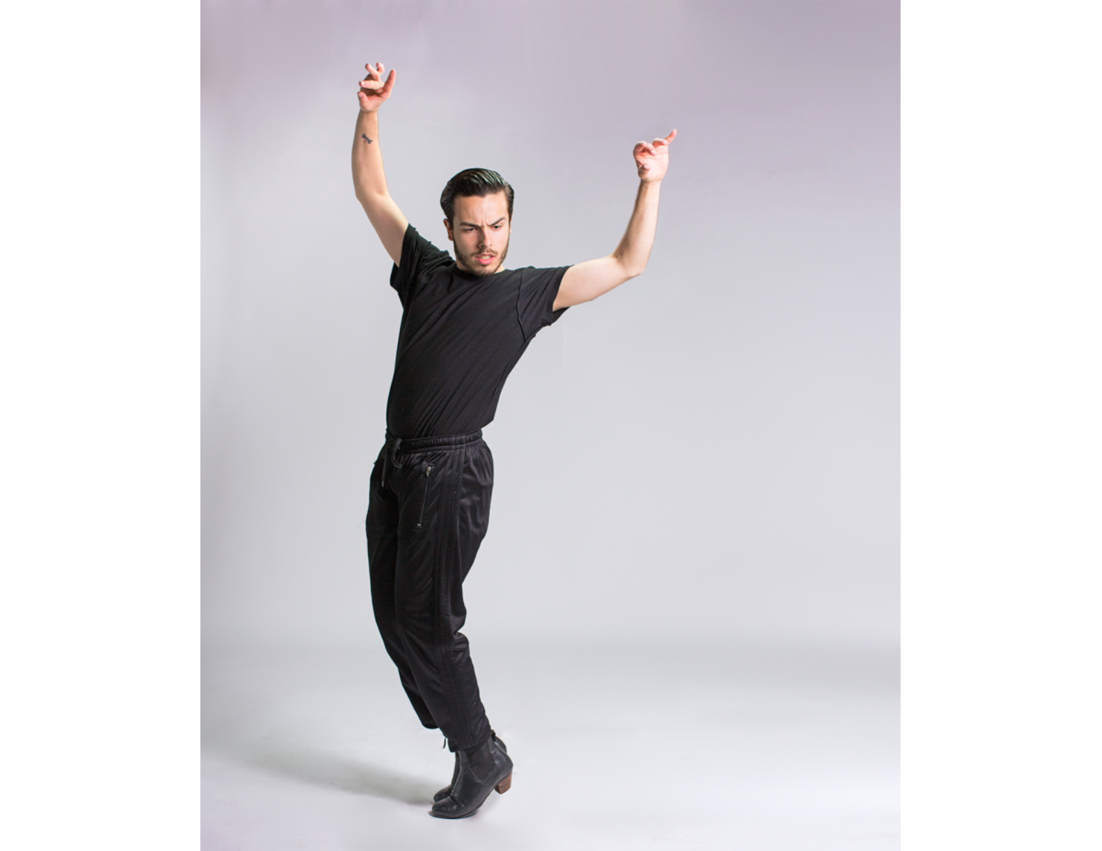male dancer wearing all black standing with his arms lifted side