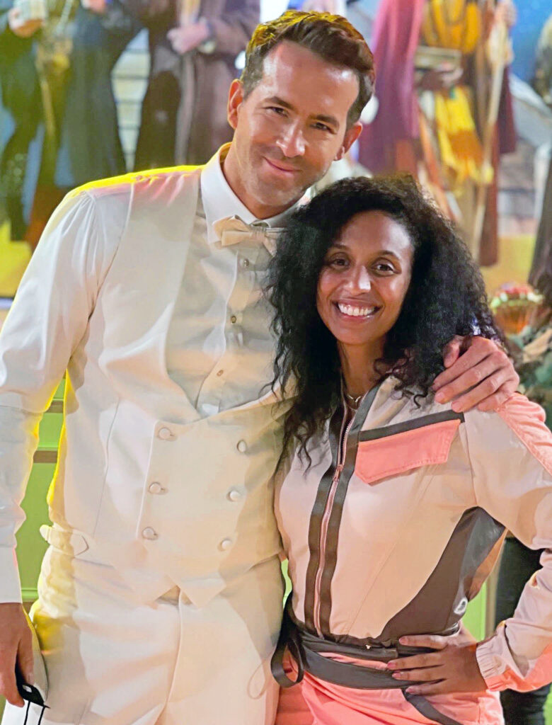 a tall man wearing a white suit with his arm around a woman with dark hair